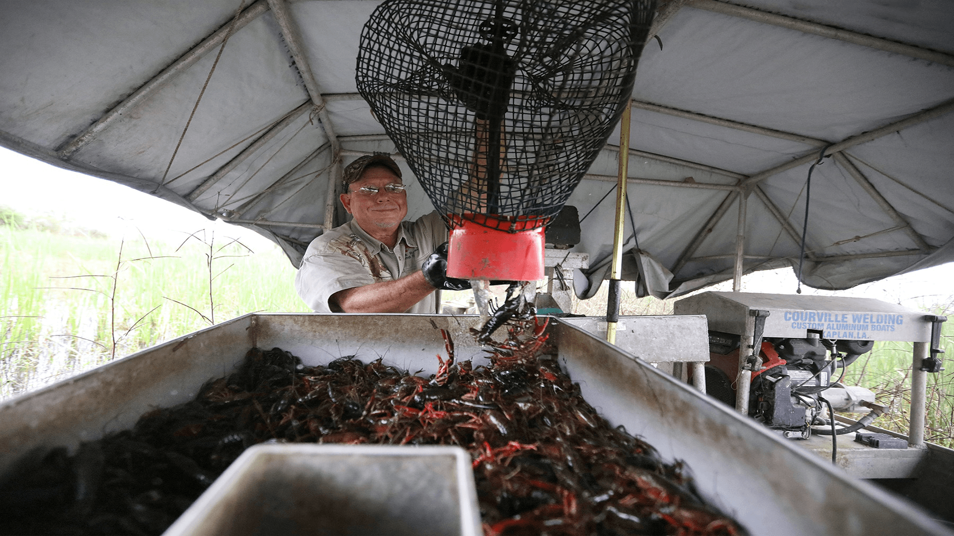 A man smiles while operating a device to sort crawfish under a tent.