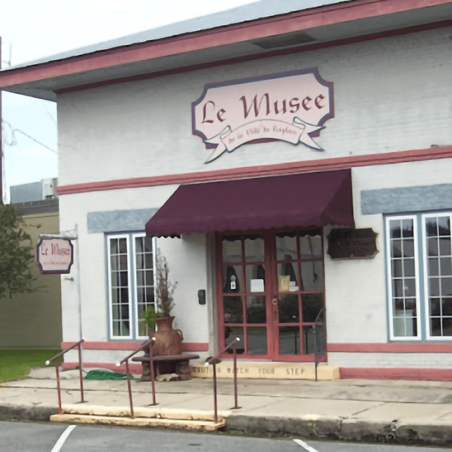 Front view of a building labeled "Le Musee," featuring a maroon awning and decorative signage.