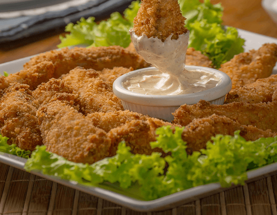 A plate of crispy breaded chicken tenders surrounded by lettuce and served with a small bowl of creamy dipping sauce.