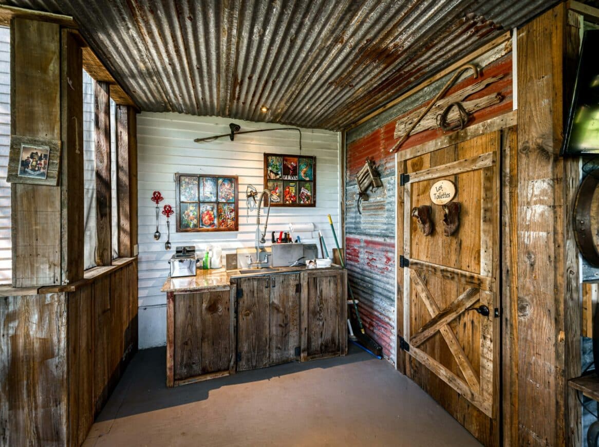 Interior of a rustic kitchen featuring wooden cabinetry, a vintage door, and colorful artwork on the walls.