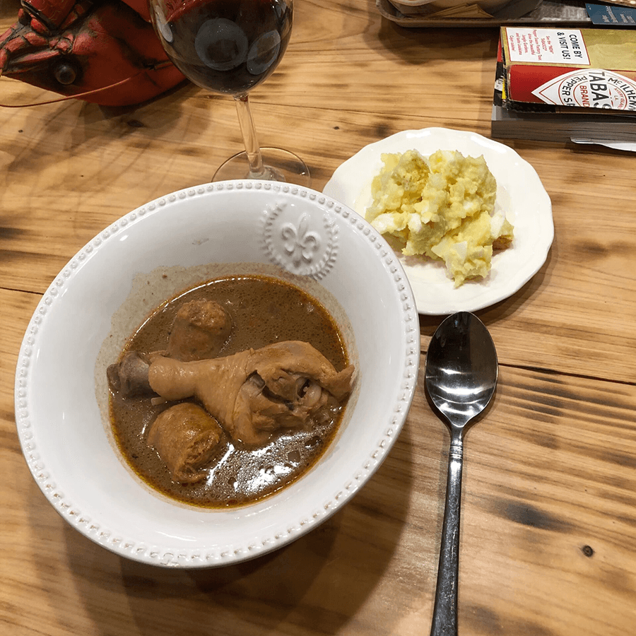 A bowl of chicken stew with a side of mashed potatoes, accompanied by a glass of red wine.