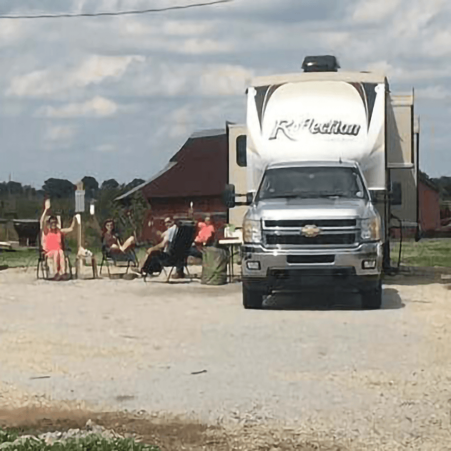 A group of people relaxes in chairs outside an RV on a sunny day.