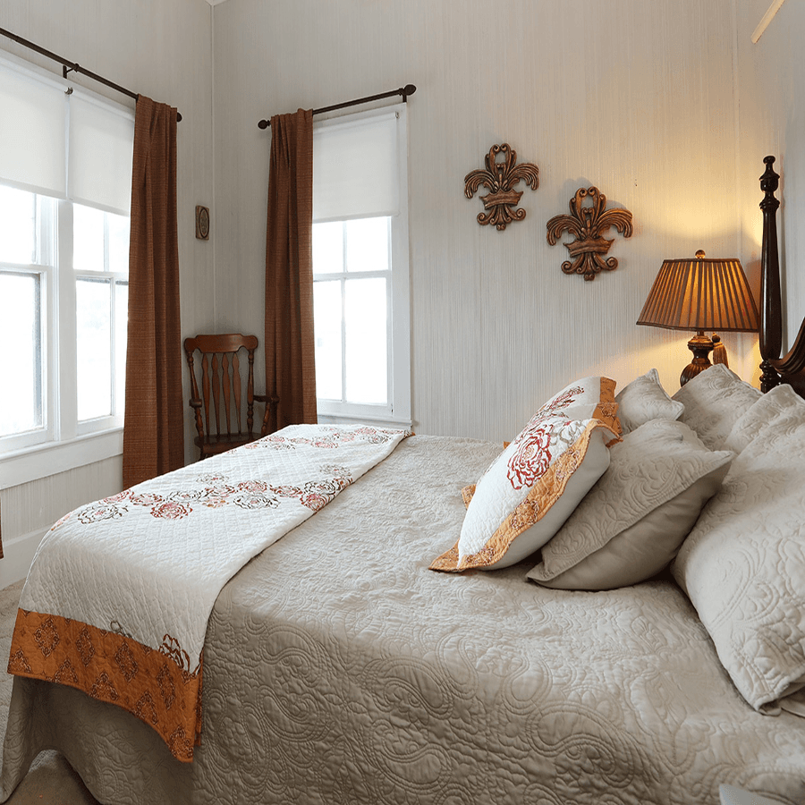 A cozy bedroom featuring a neatly made bed, decorative pillows, and warm-toned curtains.