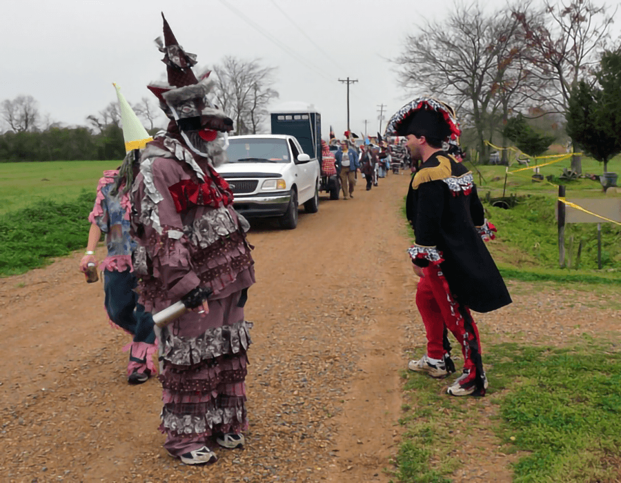 A colorful parade featuring performers in elaborate costumes on a rural road.