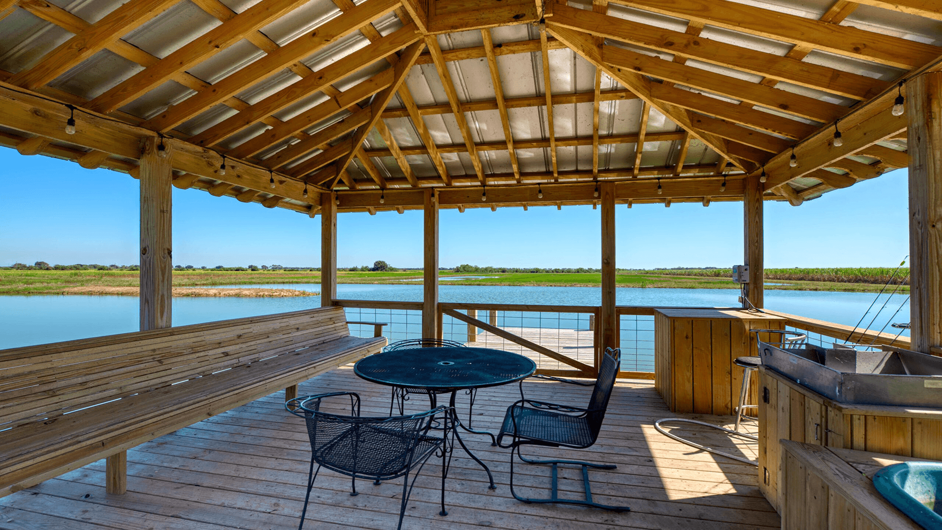 Wooden gazebo overlooking a serene waterway with seating and a table.