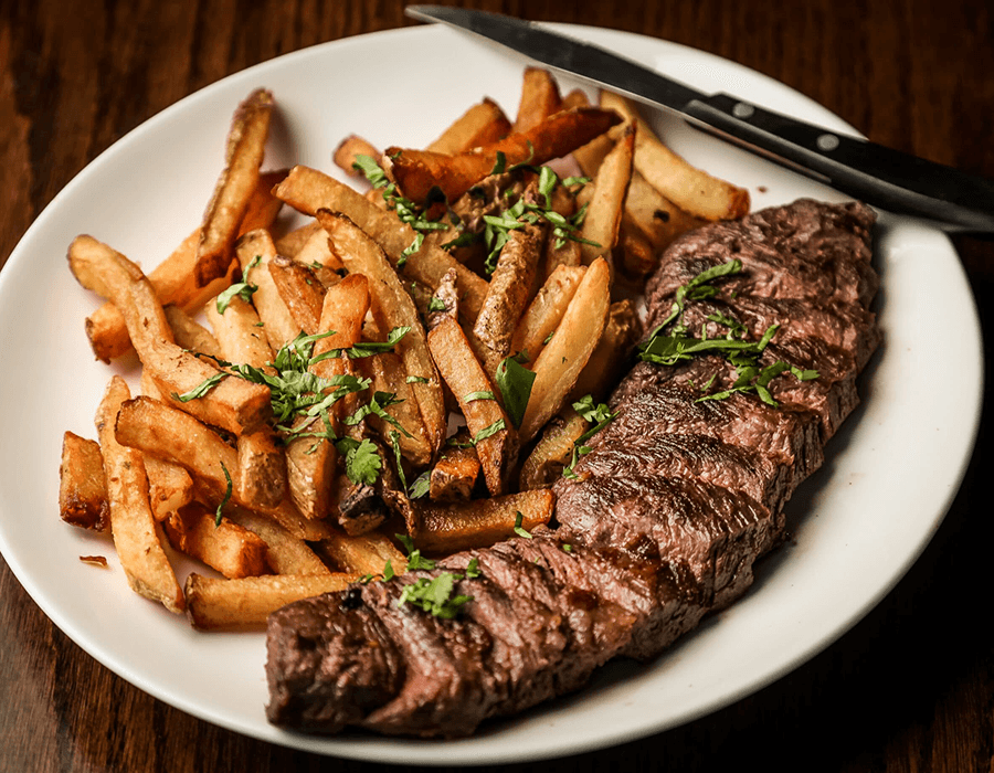 A plate of grilled steak served with seasoned French fries.