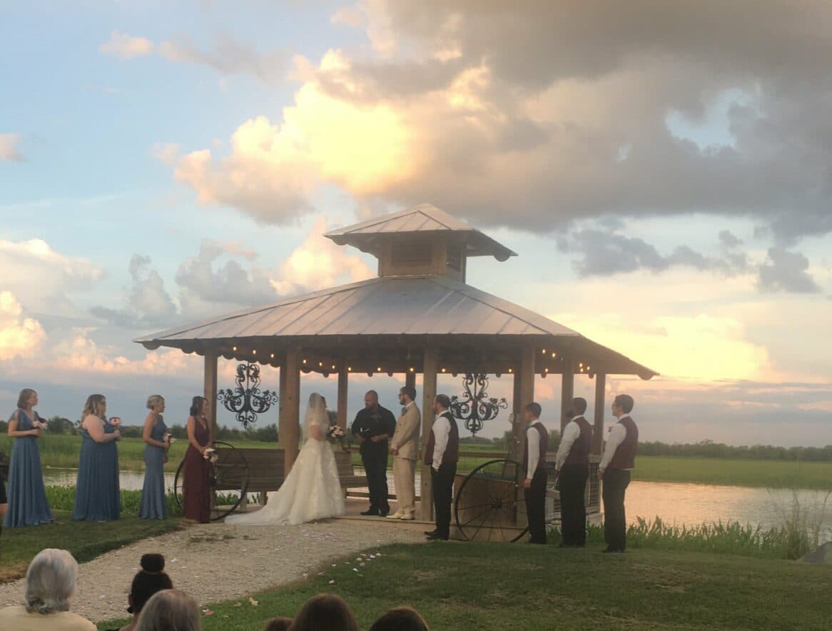A bride and groom exchange vows under a gazebo at a scenic outdoor wedding.